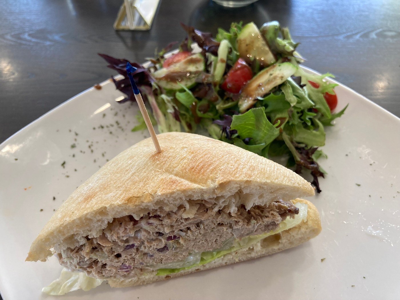 Sandwich portion with lettuce and shredded filling beside a mixed salad on a white square plate